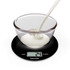 Glass bowl with milk being poured, shown on a black Salter digital kitchen scale.