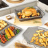 Set of non-stick roasting trays with roast chicken, vegetables and potato wedges on a kitchen worktop