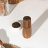 Walnut wood pepper mill upright on white worktop beside small bowl of black peppercorns