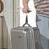 Silver hard shell suitcase held by strap, shown at home doorway