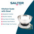 Digital kitchen scale with metal bowl holding flour, next to eggs and rolling pin