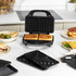 Black 3-in-1 sandwich maker open with waffle plates, shown on kitchen counter with waffles, toasties and sandwiches.