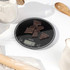 Digital kitchen scale with dark chocolate pieces on top, black glass surface, baking context