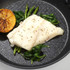 Cooked white fish fillet with spinach, asparagus, and grilled lemon in a non-stick frying pan