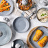 Set of grey non-stick frying pans and pots with food, shown on kitchen surface