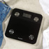 Black digital bathroom scale with silver sensors on tiled floor