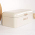 Cream metal bread bin with rose gold handle and embossed 'BREAD' lettering, shown on kitchen counter