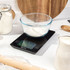 Digital kitchen scale with glass bowl of flour on worktop, black display, baking setting