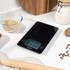 Slim black digital kitchen scale in a drawer with wooden utensils beside it
