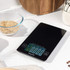 Black digital kitchen scale with touchscreen display on worktop, shown in kitchen setting