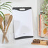 White plastic chopping board with black edges, shown upright on kitchen counter
