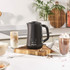 Black Salter milk frother on kitchen counter, shown with coffees and hot chocolate.