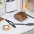 Cooked beef roast on a white chopping board with knife, salt and pepper pots nearby