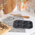 Six-cup black non-stick muffin tray on striped tea towel in kitchen setting