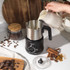 Milk frothing jug pouring steamed milk into cappuccino with foam and cocoa topping