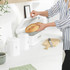 Kitchen scene with hand taking tea from white canister, next to mug and fresh bread