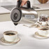 Stainless steel electric kettle pouring hot water into cup on kitchen counter
