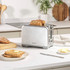 Silver electric kettle with visible water gauge and blue power switch being pressed