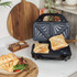 Black sandwich toaster with two toasted sandwiches on kitchen counter
