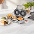 Silver pie maker with two baked pies, beside plate of pie, chips, peas and ketchup.
