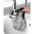 Glass electric kettle with silver accents being filled with water at a kitchen sink