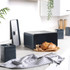 Set of black metal kitchen storage canisters on worktop with bread and butter in foreground
