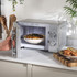 Silver microwave oven with open door and white bowl inside, shown from the front.