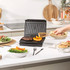 Black panini press shown grilling a filled ciabatta sandwich on kitchen counter