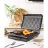 Electric grill with steak and vegetables cooking on kitchen counter, hand using spatula