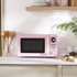 Light pink microwave oven on countertop, hand turning dial, chocolate pieces in foreground