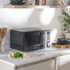 Grey microwave oven on kitchen counter, person setting timer with hand, plate and fork beside.