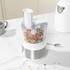 White food processor with clear bowl chopping mixed vegetables on a kitchen counter