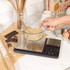 Baking scales with glass bowl of brown sugar, hand shown, kitchen counter scene.