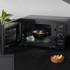 Black microwave oven with door open, bowl of hot soup inside, on kitchen counter