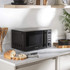 Black digital microwave oven with blue LED display, hand turning control knob, on kitchen counter