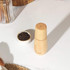 Wooden pepper grinder on kitchen counter beside bowl of black peppercorns