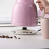Pink 4-slice toaster with controls, two seeded bread slices toasting, hand pressing lever