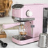 Pink espresso coffee machine in kitchen making coffee, shown with milk jug and scoop.