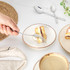 Hand holding fork with cake slice and cream on ceramic plate, coffee and cutlery nearby.