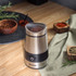 Stainless steel coffee grinder with lid open and whole coffee beans inside, on wooden surface