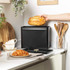 Black metal bread bin with lid open, loaf inside, on modern kitchen counter