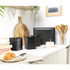 Set of black kitchen storage canisters in modern kitchen, shown with bread bin, tea, coffee and sugar jars.