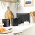 Set of black kitchen storage canisters in modern kitchen, shown with bread bin, tea, coffee and sugar jars.