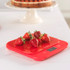 Red digital kitchen scale with strawberries on top, shown on a kitchen countertop