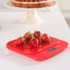 Red digital kitchen scale with strawberries on top, shown on a kitchen countertop