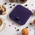 Digital kitchen scale in dark blue with display, surrounded by muffins and blueberries