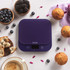 Purple digital kitchen scale on countertop with muffins, berries and coffee