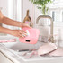 Person cleaning pink digital kitchen scale under running tap in modern sink