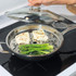 Stainless steel steamer basket in frying pan on hob, steaming fish and asparagus