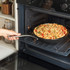 Hand placing oven-safe pan with baked pasta in electric oven